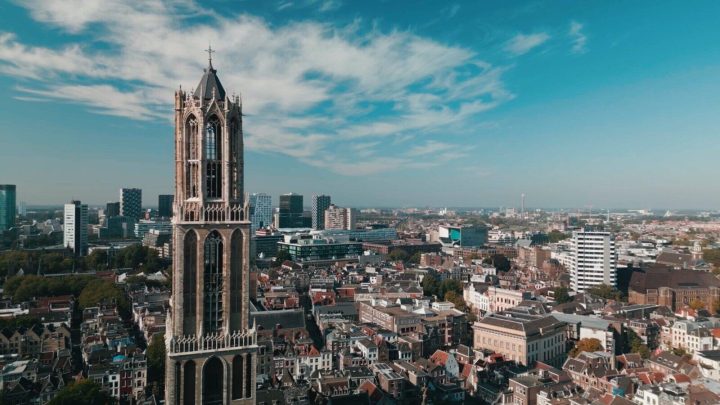 Luchtfoto van de Domtoren boven de daken van de Utrechtse binnenstad, met moderne hoogbouw op de achtergrond.